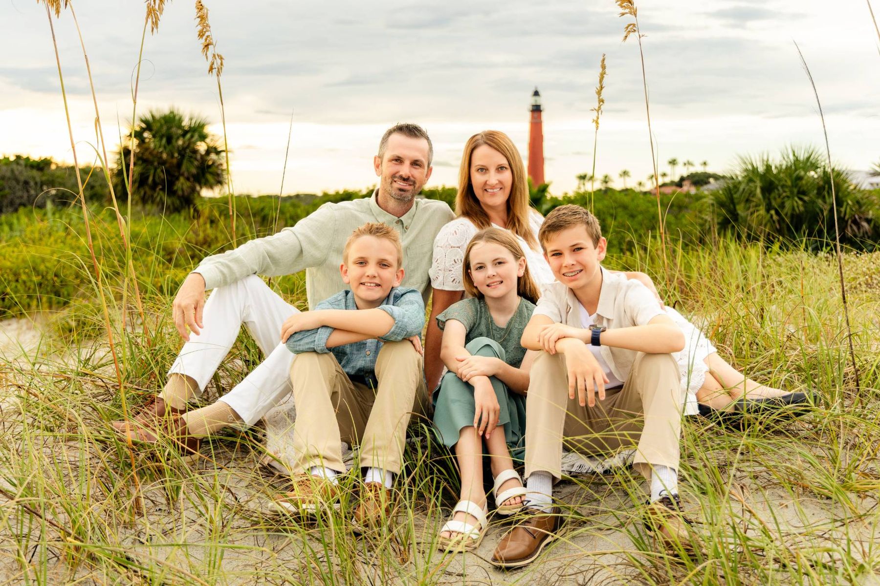 Caleb Tidwell and his family sitting together in the sea oats with a lighthouse behind them