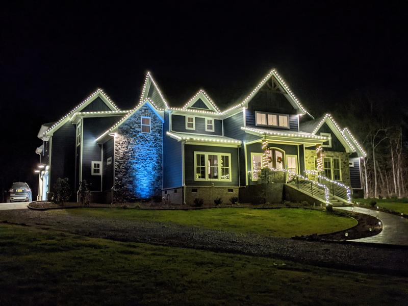 Modern farmhouse with white lights on the roofline and blue uplighting