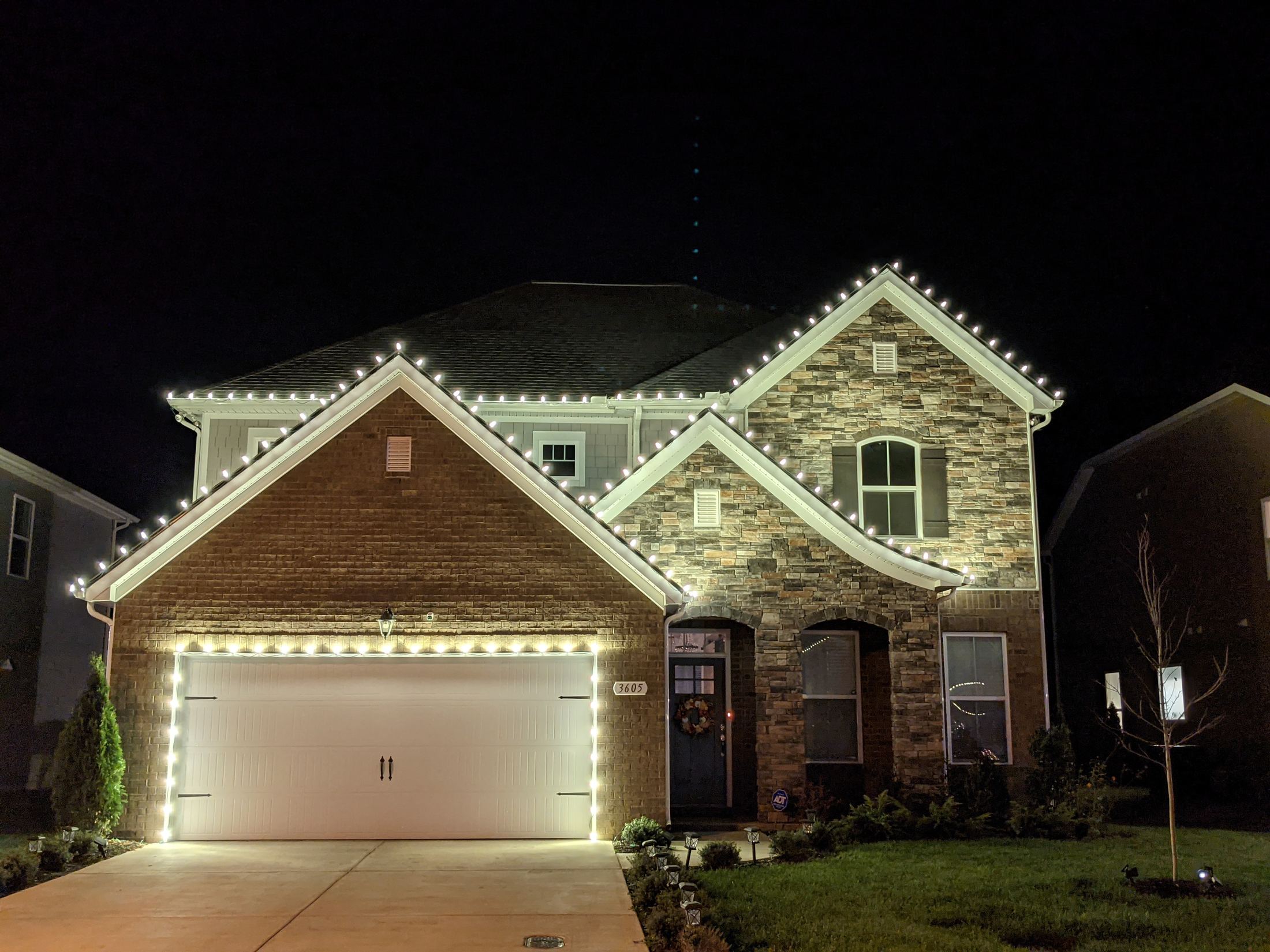 Brick home with a white garage door and lights outlining each gable