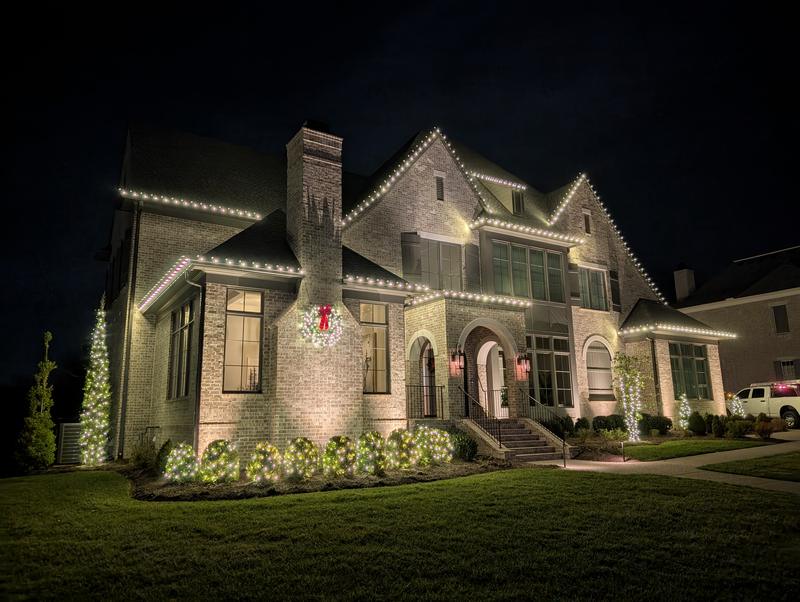 Large home with wreaths and a lit garden bed