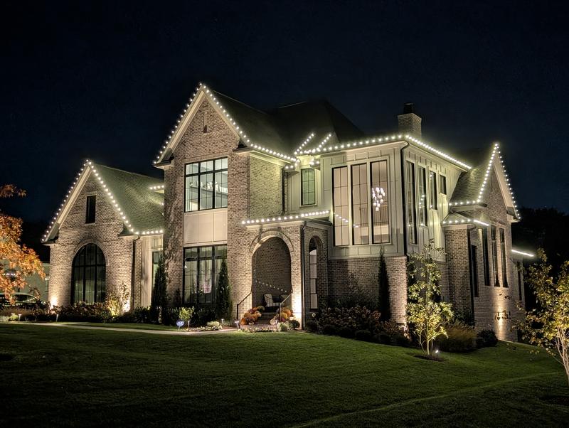 Brick and board-and-batten home with lights on every gable and peak
