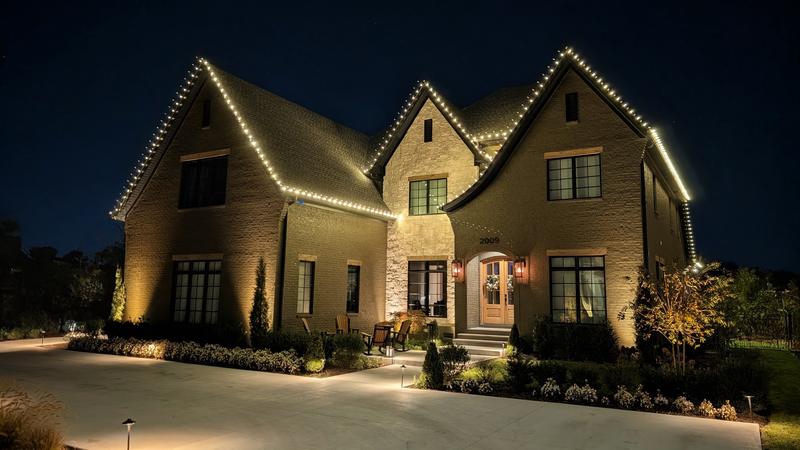 Stone and brick home with warm white lights on three tall gables
