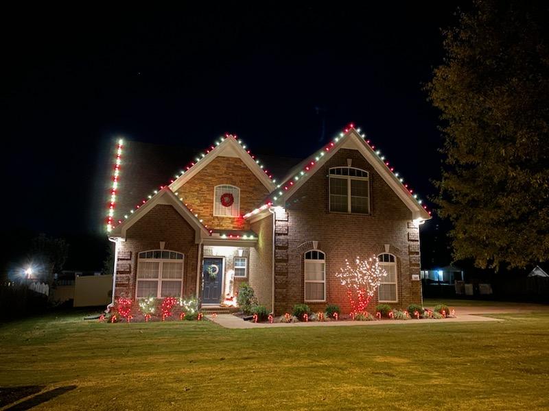 Brick home with red and white lights, wreaths and candy canes