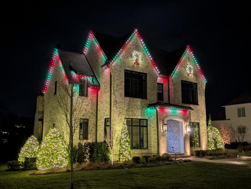 Stone home with red and green lights on every gable and wreaths