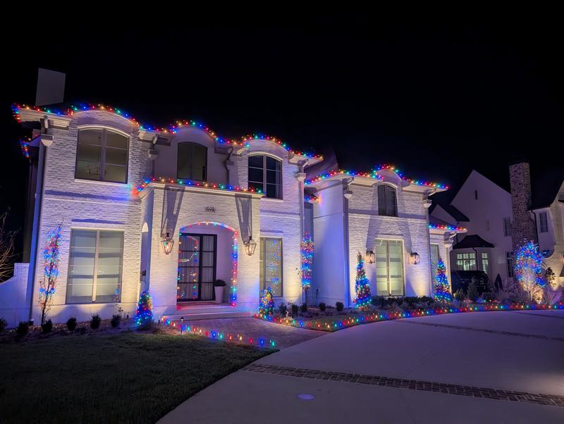 White home with multicolor lights along the roofline and front yard