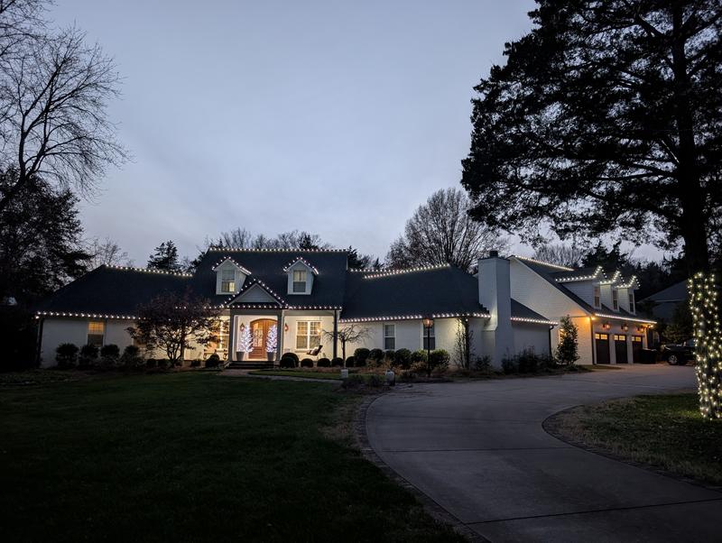 Large white home at dusk with white roofline lights and a lit tree