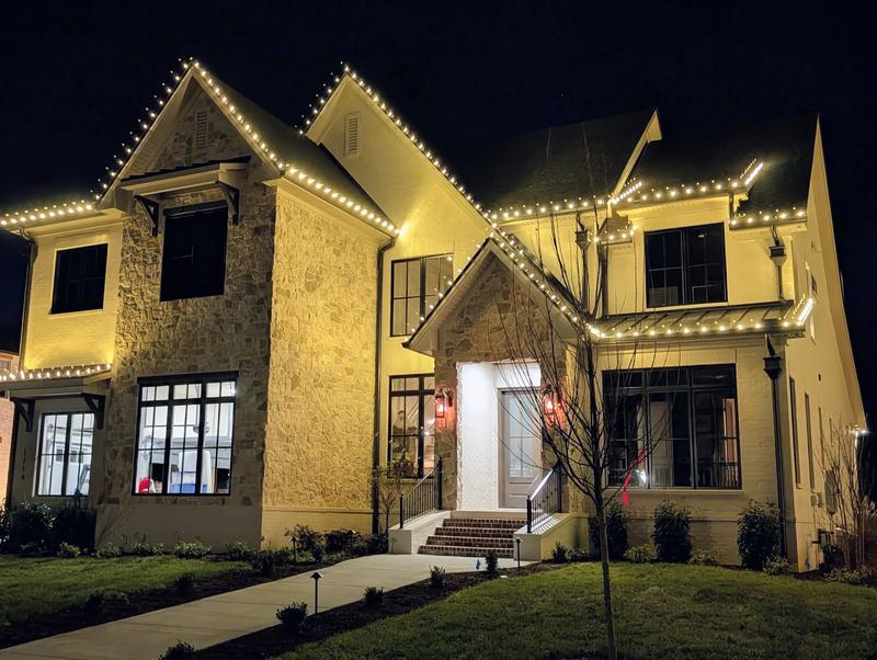 Stone and stucco home with warm white lights on every peak