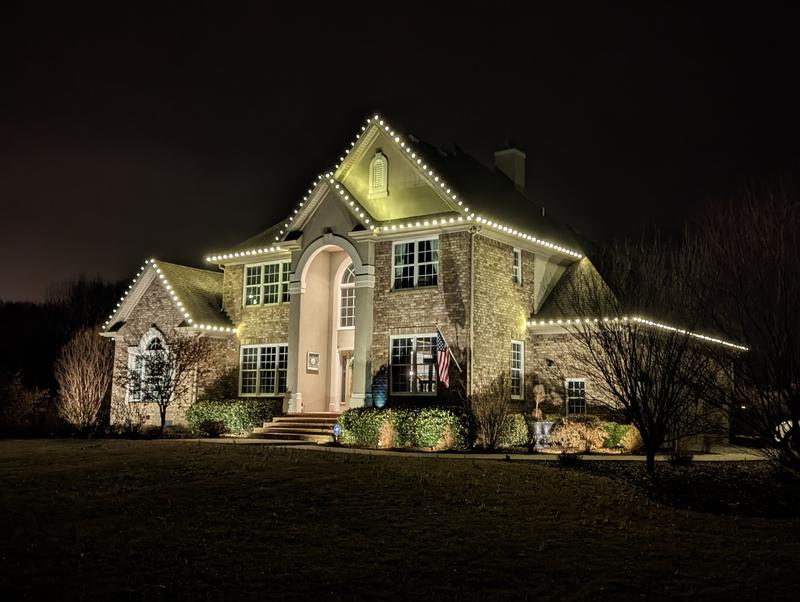Brick home with white lights on the gables and a lit arched entry