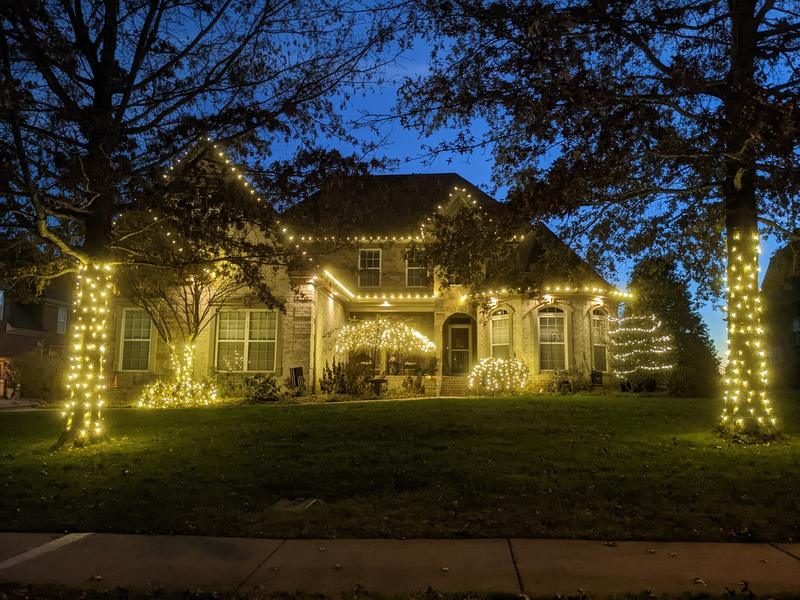 Brick home framed by two trees wrapped in warm white lights