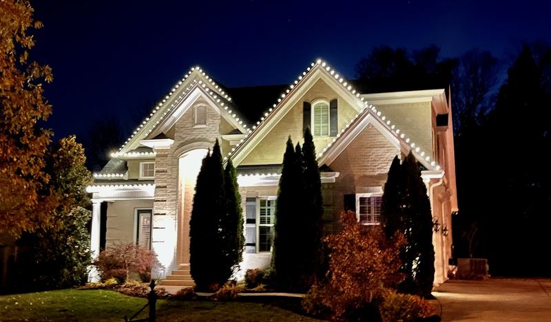 Two-story home with warm white lights on every gable and uplit columns