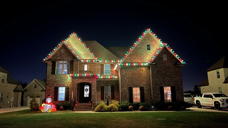 Brick home with red and green lights tracing both gables