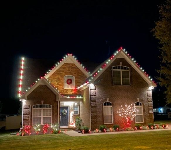 Brick home with red and white lights on the roofline and a lit wreath