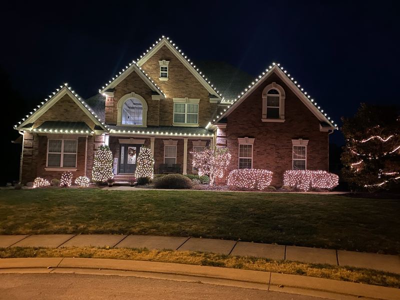 Large brick home with white lights on every gable and lit shrubs