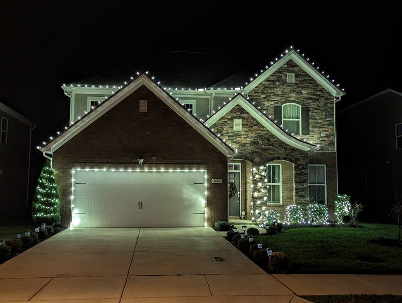 Stone and brick home with white lights on every peak and around the garage door