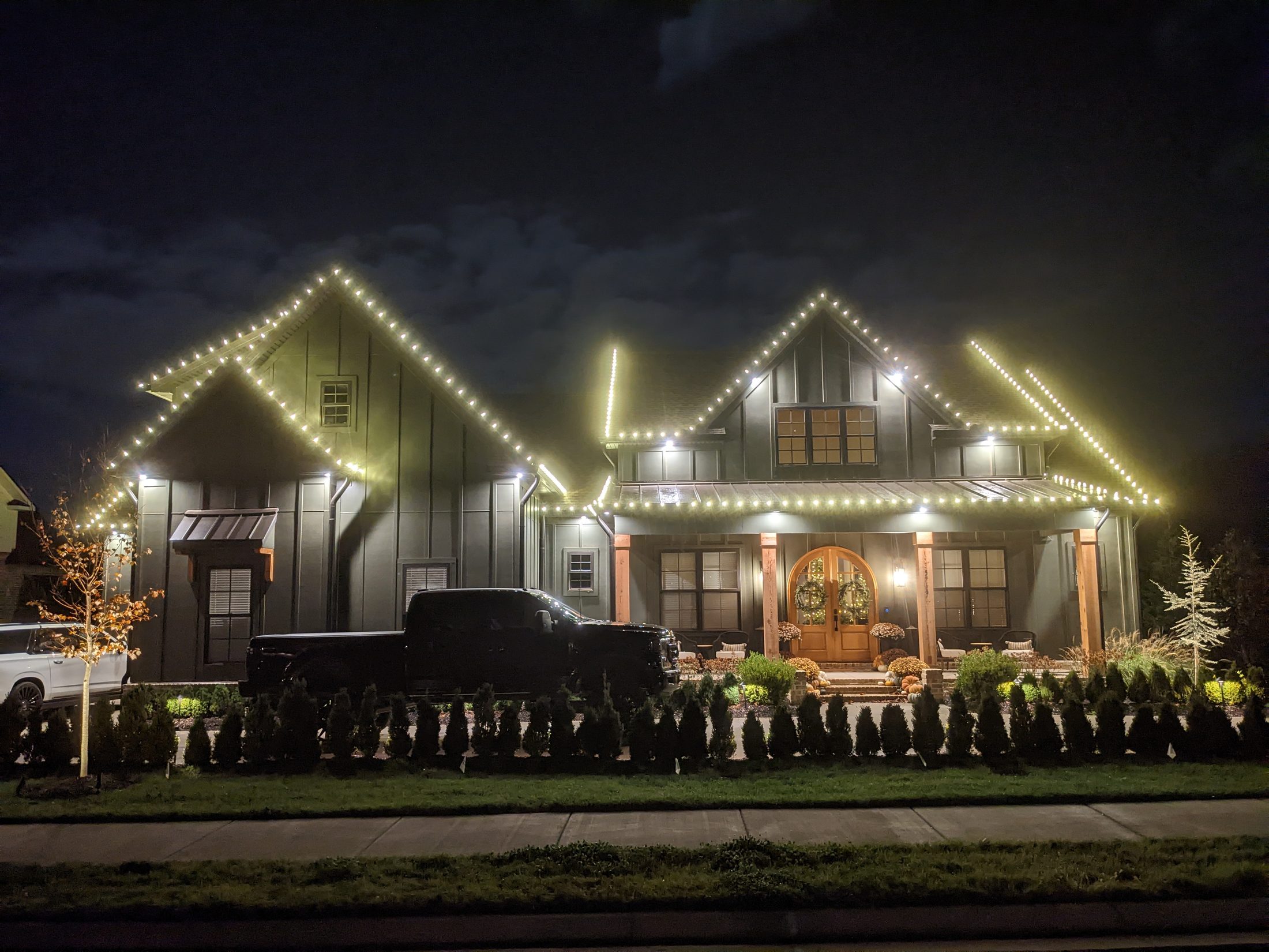 Modern farmhouse with warm white lights on every gable and porch at dusk