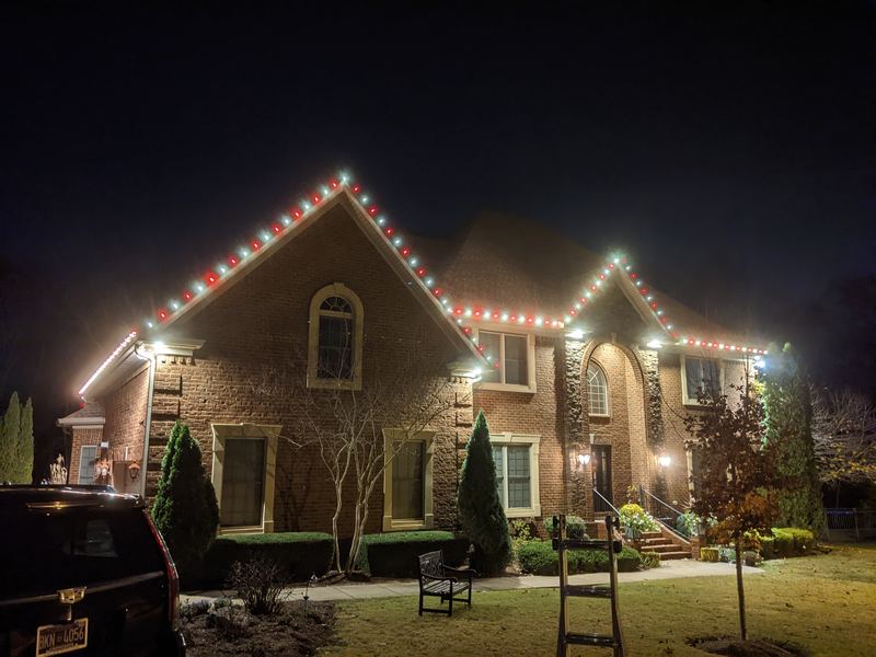 Brick home with red and white lights on the roofline and lit trees